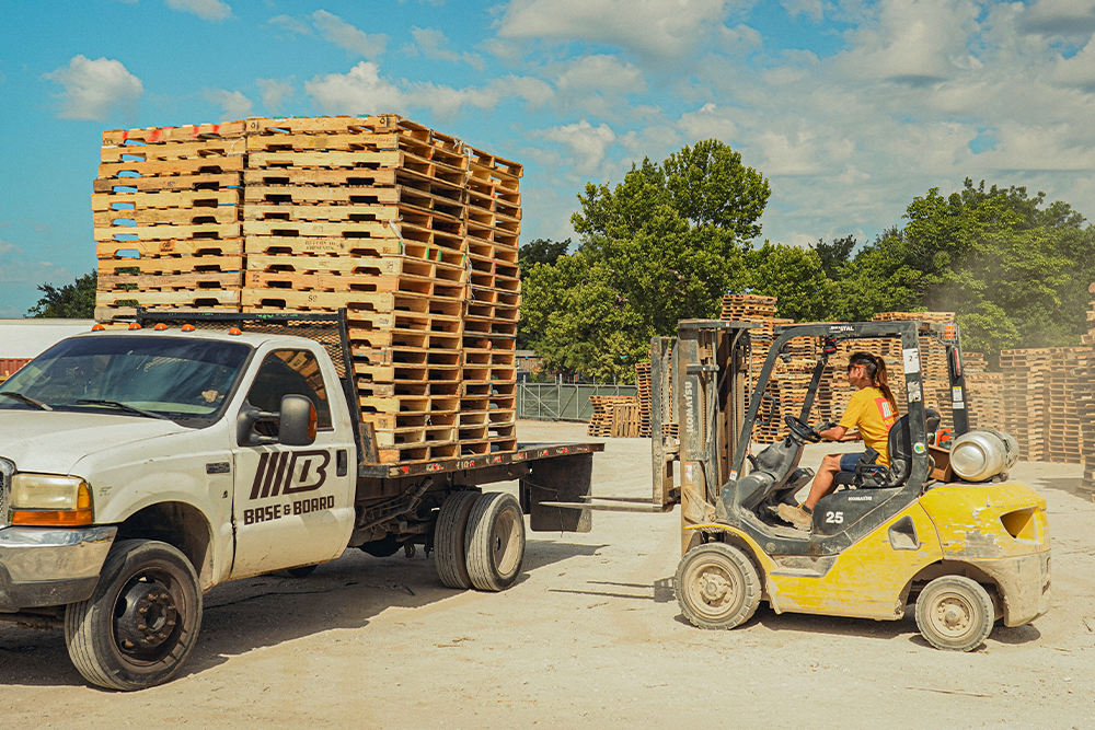 Stack of wooden pallets on a truck and forklift at a loading dock.