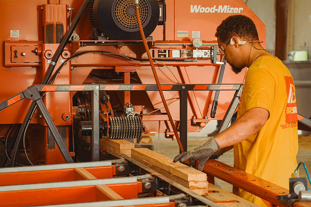 Worker operating a woodworking machine with lumber on a conveyor.