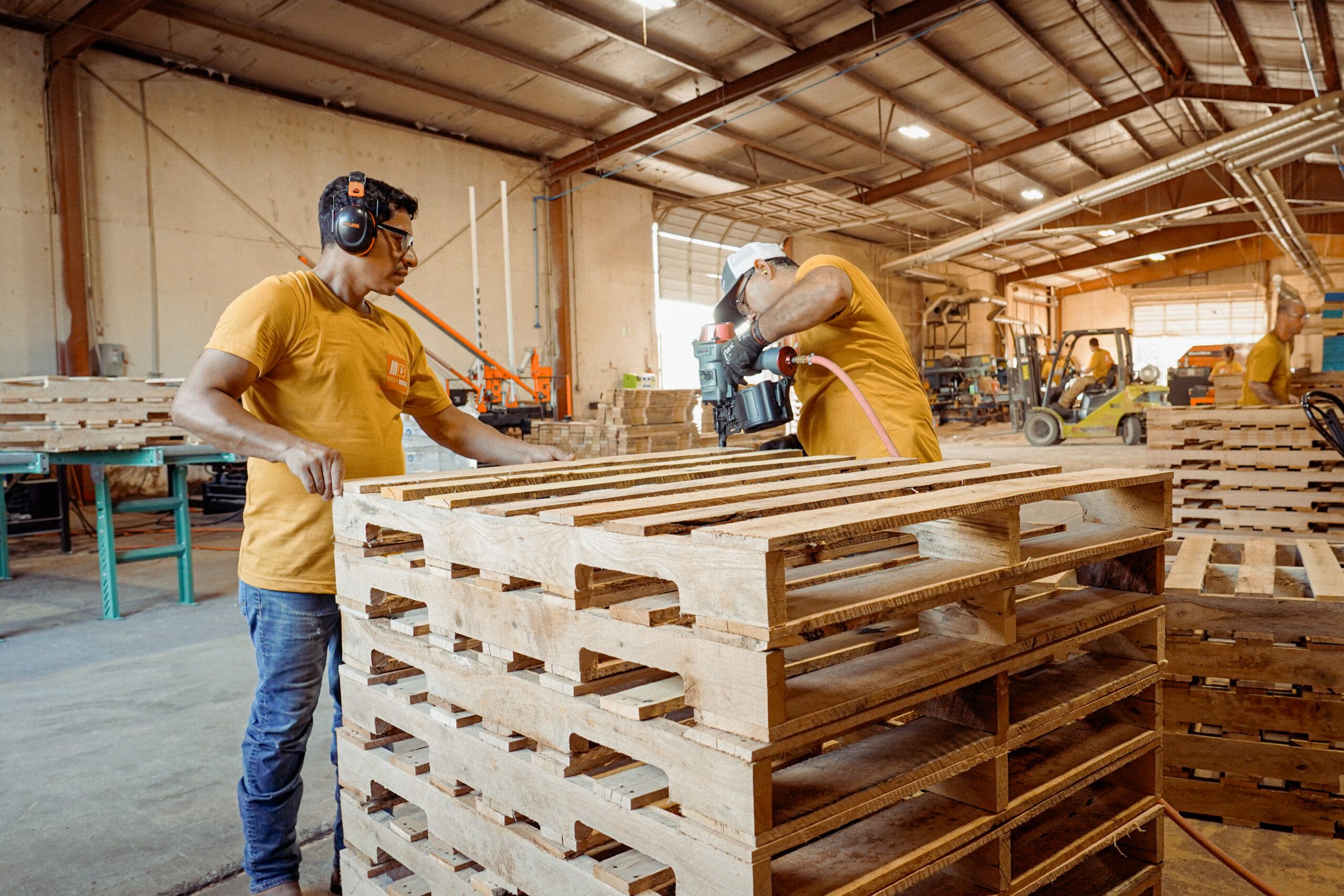 Workers assembling wooden pallets in a warehouse setting.