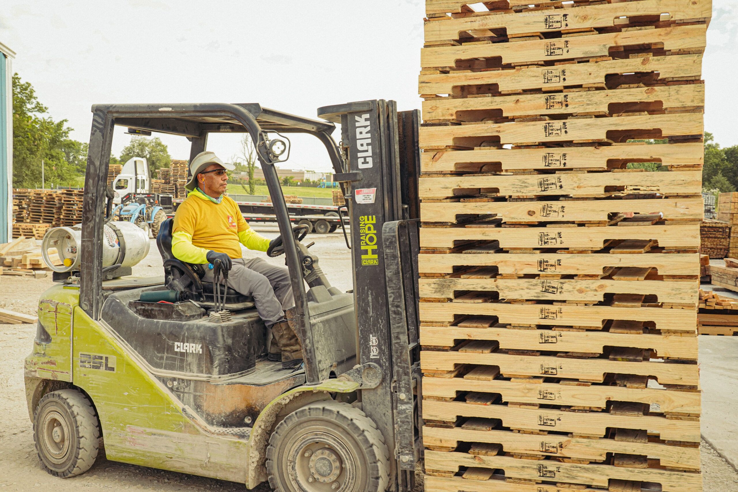Forklift stacking wooden pallets at a loading dock. Pallets are stacked.